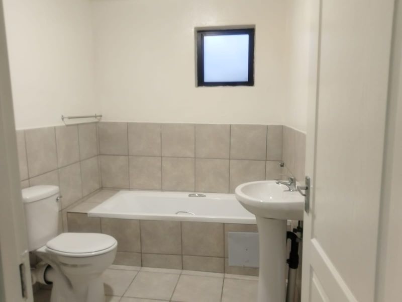 A functional bathroom featuring a built-in bathtub, pedestal basin, and toilet with neutral wall and floor tiling.