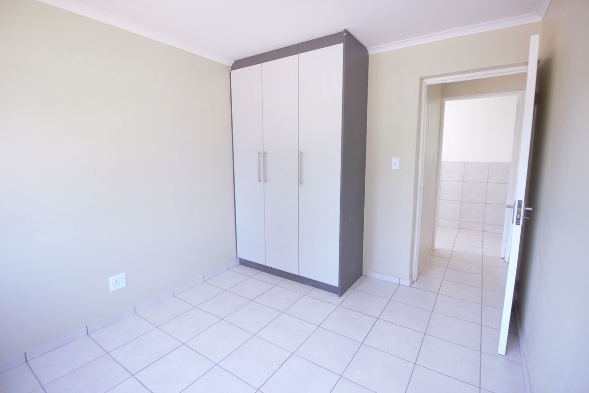 A clean, empty bedroom featuring neutral tiled flooring, a modern built-in wardrobe, and access to an adjacent tiled space.