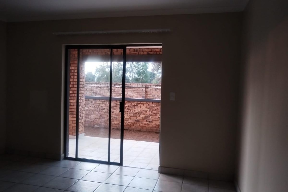 An empty living area featuring neutral tiled flooring and a sliding glass door providing direct access to an outdoor patio space.