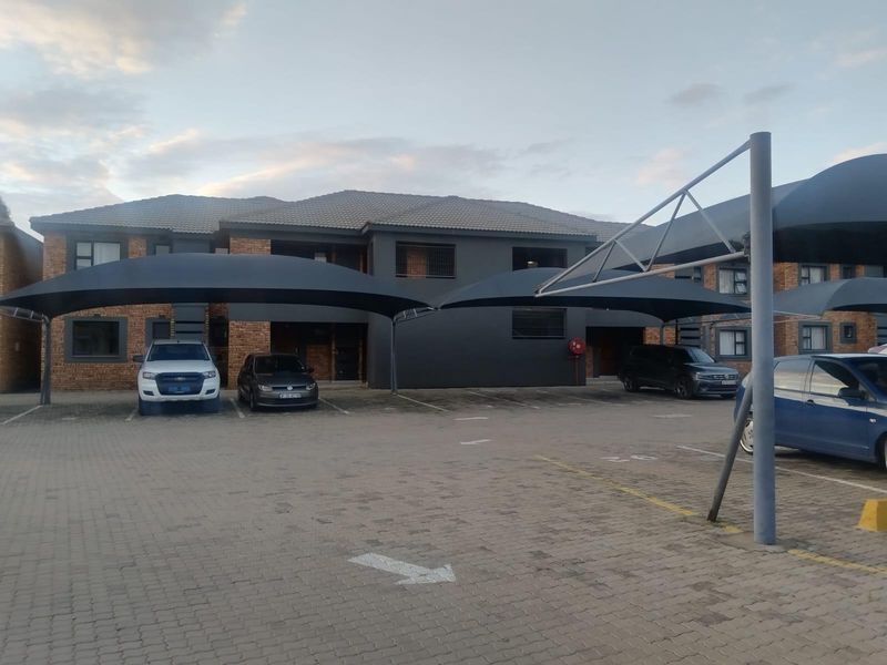 Front exterior view of the townhouse complex featuring a paved parking area with installed shade cloth carports and a modern dark-painted brick facade.
