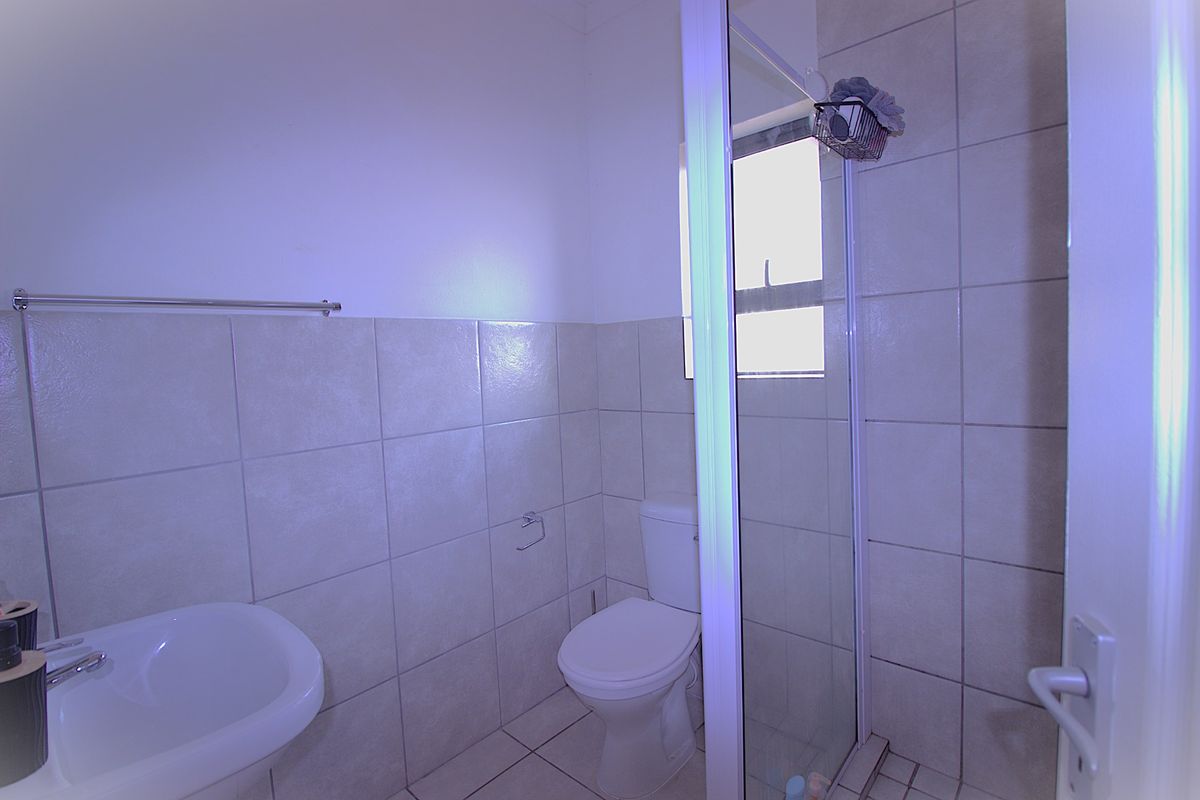 A functional bathroom featuring a shower enclosure, pedestal basin, and toilet with neutral wall and floor tiling.