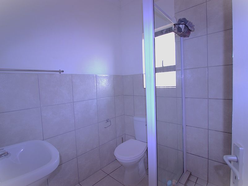 A functional bathroom featuring a shower enclosure, pedestal basin, and toilet with neutral wall and floor tiling.