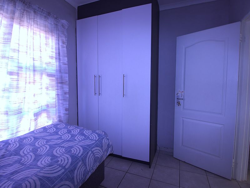 A bedroom featuring tiled flooring and a built-in wardrobe with modern handles, offering functional storage space.