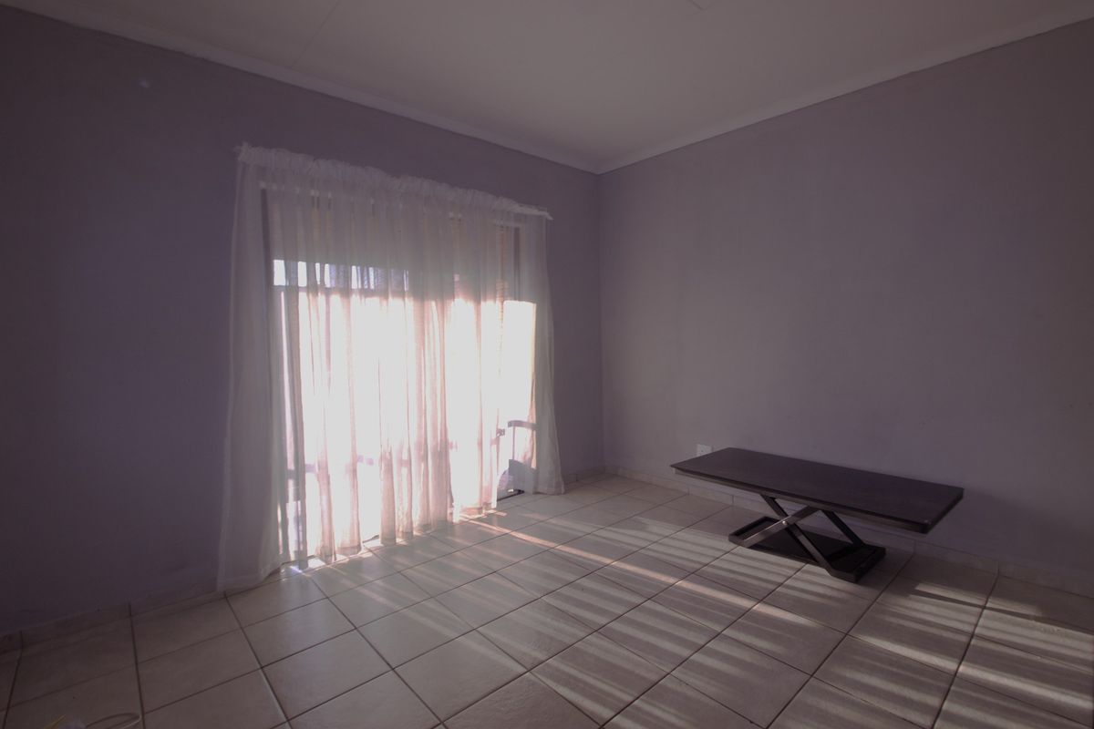 A bright, empty living room featuring neutral wall paint, tiled flooring, and a large sliding glass door providing natural light.
