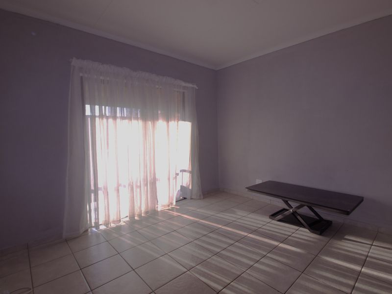 A bright, empty living room featuring neutral wall paint, tiled flooring, and a large sliding glass door providing natural light.