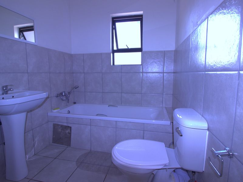 A functional bathroom featuring a pedestal basin, a built-in bathtub with shower attachment, and a standard toilet, finished with neutral wall and floor tiles.
