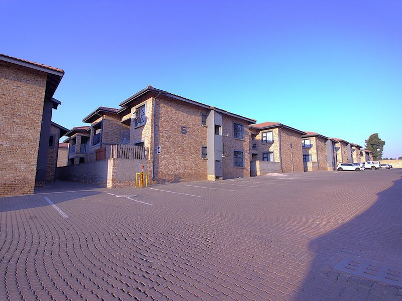 Exterior view of a multi-unit apartment complex featuring face brick construction, tiled roofs, and a spacious paved parking area.