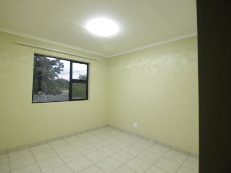 An empty bedroom featuring tiled flooring, neutral wall paint, and an aluminium window frame with a curtain rail.