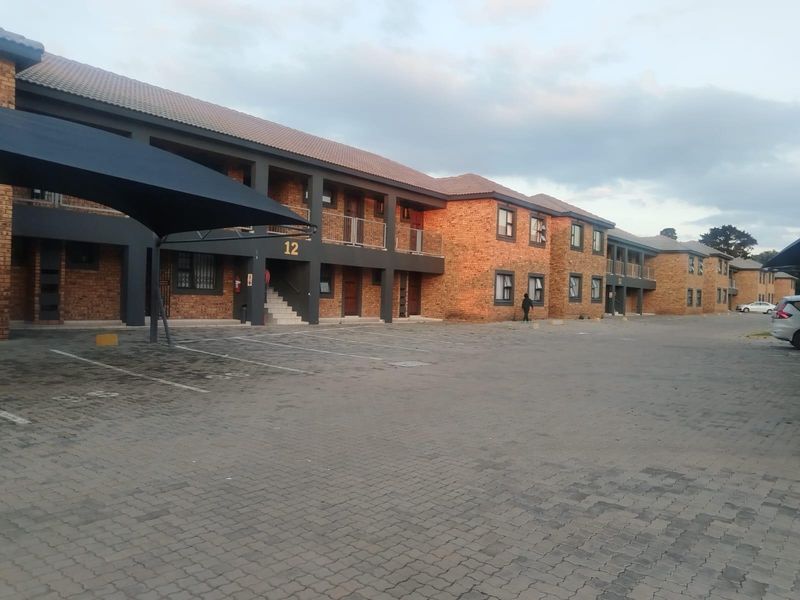 Exterior view of a multi-story townhouse complex featuring face brick construction, paved parking areas, and covered carports.