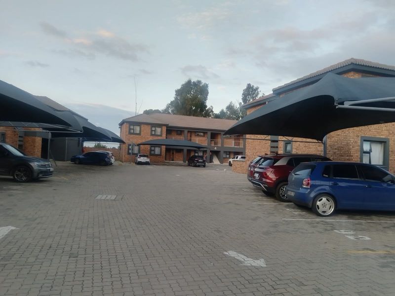 Exterior view of a townhouse complex featuring facebrick buildings, paved parking areas, and installed shade cloth carports.