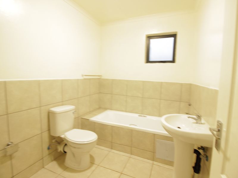 A functional bathroom featuring a pedestal basin, a built-in bathtub, and a toilet, finished with neutral wall and floor tiling.