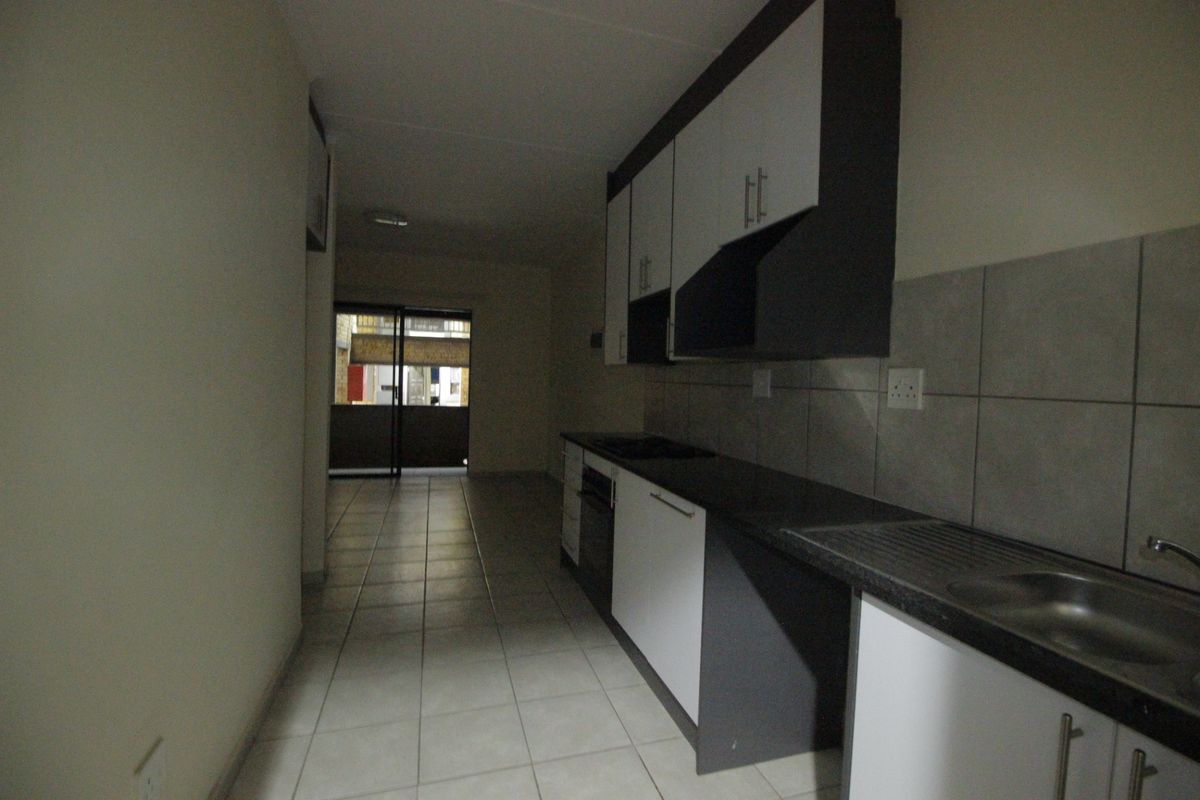 A galley-style kitchen featuring built-in cabinetry, laminate countertops, a stainless steel sink, and tiled flooring, leading towards an exterior balcony.