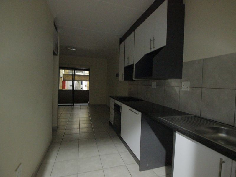 A galley-style kitchen featuring built-in cabinetry, laminate countertops, a stainless steel sink, and tiled flooring, leading towards an exterior balcony.