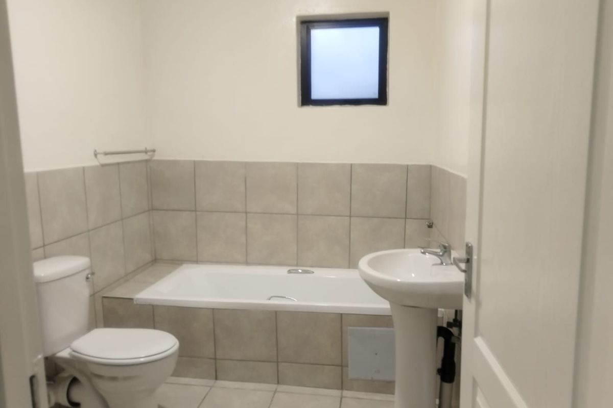 A functional bathroom featuring a built-in bathtub, pedestal basin, toilet, and neutral ceramic tiling throughout.