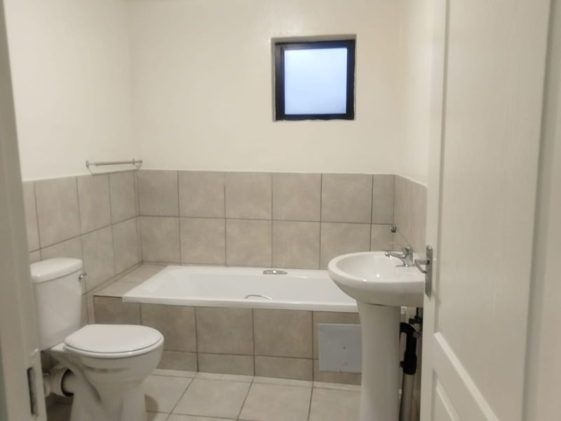 A functional bathroom featuring a built-in bathtub, pedestal basin, toilet, and neutral ceramic tiling throughout.
