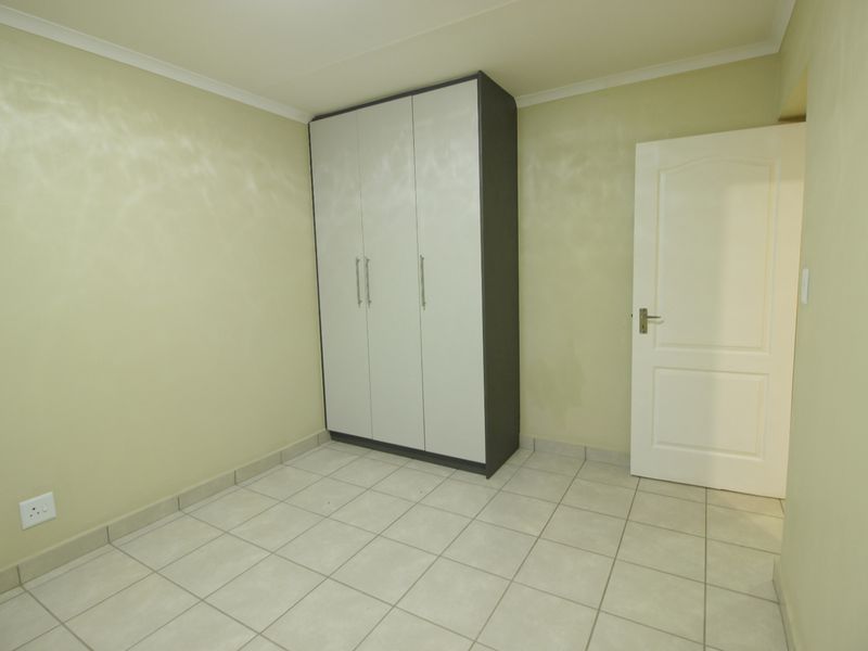 A vacant bedroom featuring neutral tiled flooring, built-in wardrobe storage, and light-colored walls, offering a clean canvas for personalization.