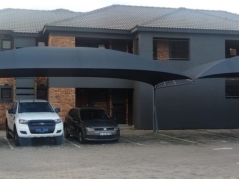 Front exterior view of the townhouse complex featuring a paved parking area with shade cloth carports and a combination brick and rendered facade.