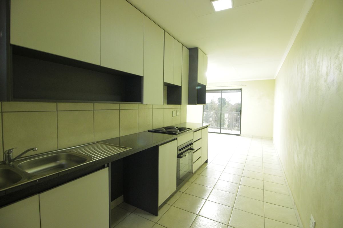 A clean, modern kitchen featuring built-in cabinetry, a stainless steel sink, integrated oven and hob, and tiled flooring leading to a sliding glass door.