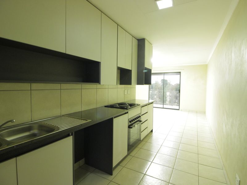 A clean, modern kitchen featuring built-in cabinetry, a stainless steel sink, integrated oven and hob, and tiled flooring leading to a sliding glass door.