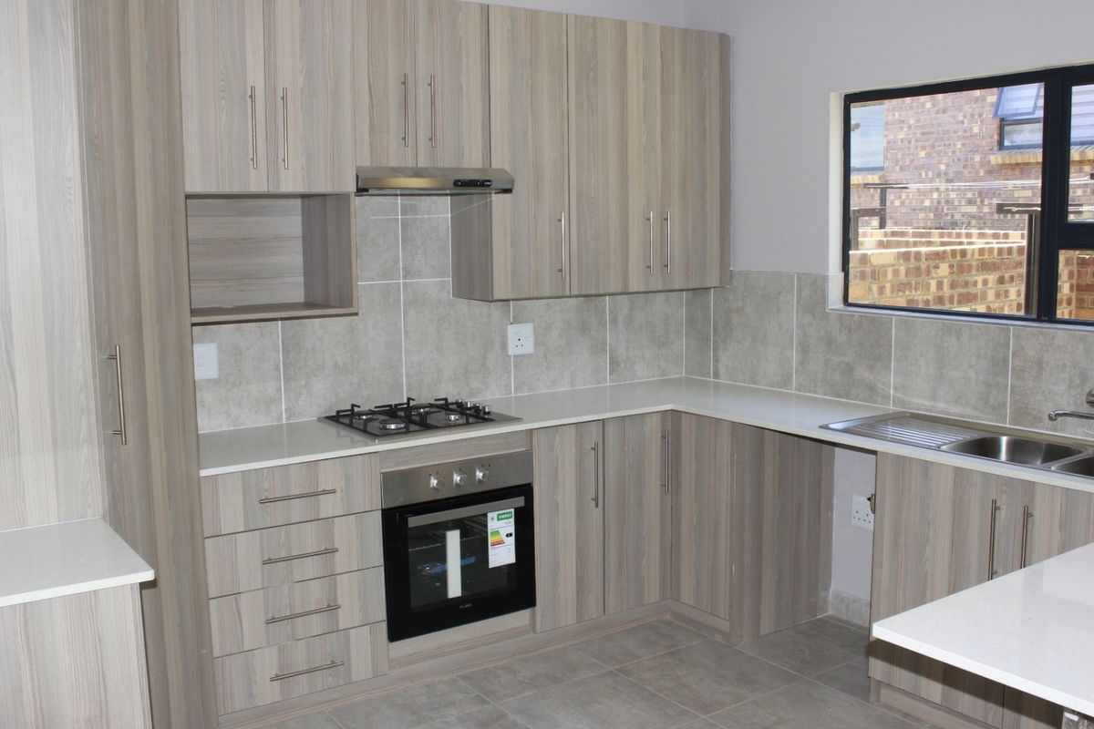 Modern kitchen featuring light wood-grain cabinetry, stone countertops, a gas hob, built-in oven, and a double bowl sink with tiled backsplash.