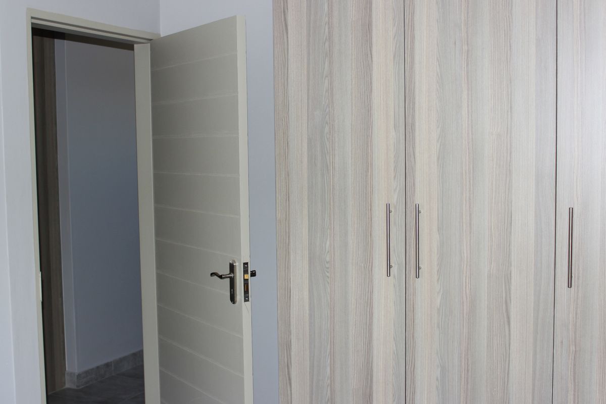 A clean bedroom interior featuring modern wood-grain built-in wardrobes and a neutral interior door.