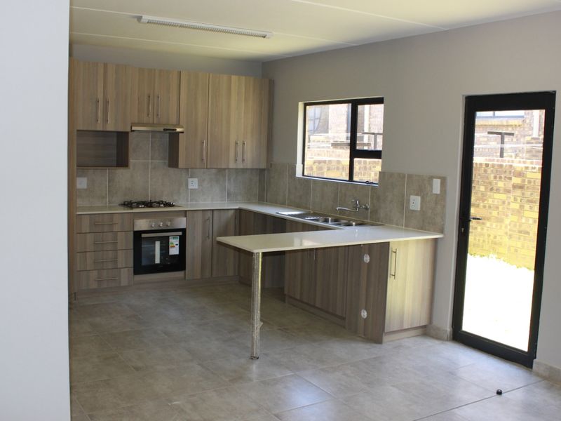 Modern kitchen featuring light wood cabinetry, stone countertops, built-in oven, gas hob, and tiled flooring, with direct access to the rear exterior.