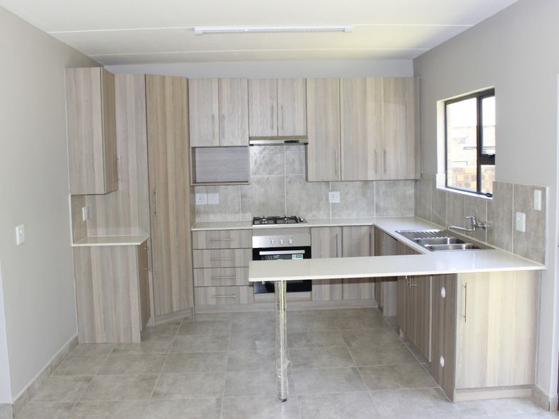 Modern kitchen featuring light wood-grain cabinetry, stone countertops, a breakfast bar, and integrated gas hob and oven, with direct access to the rear exterior.