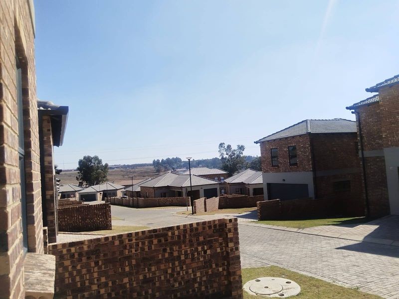 A view of a residential street within a housing estate, featuring face brick homes, paved driveways, and boundary walls under a clear sky.