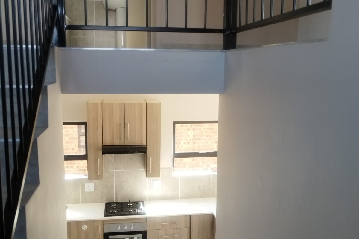 A modern kitchen featuring light wood cabinetry, a gas hob, built-in oven, and extractor fan, viewed from the staircase landing.
