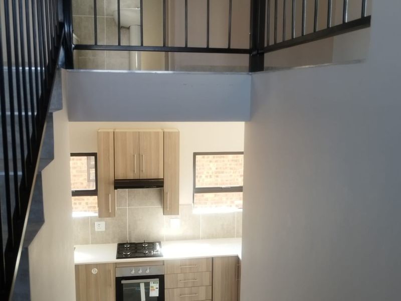 A modern kitchen featuring light wood cabinetry, a gas hob, built-in oven, and extractor fan, viewed from the staircase landing.