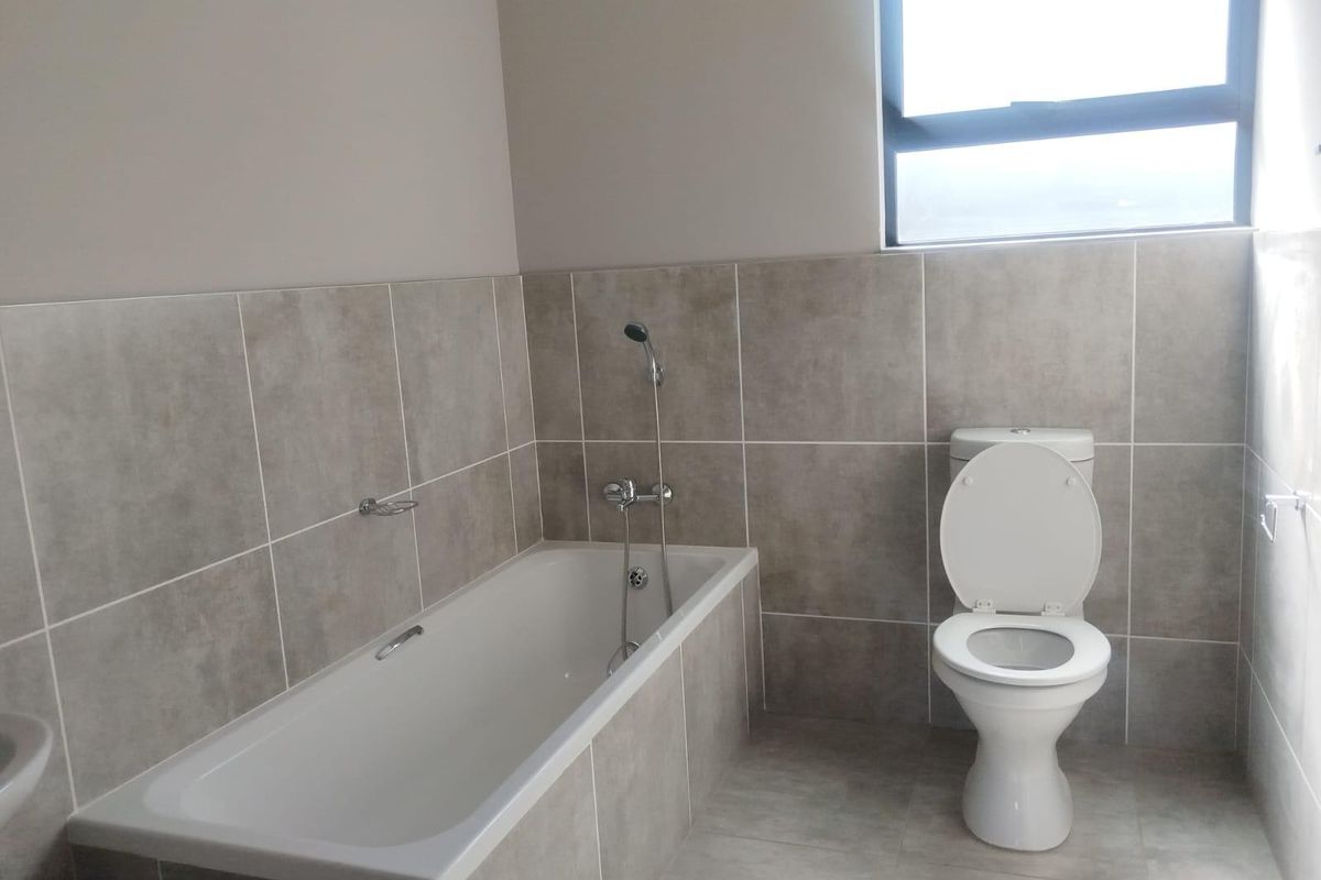 A clean, modern bathroom featuring neutral-toned wall and floor tiles, a built-in bathtub with a handheld shower mixer, and a standard ceramic toilet.