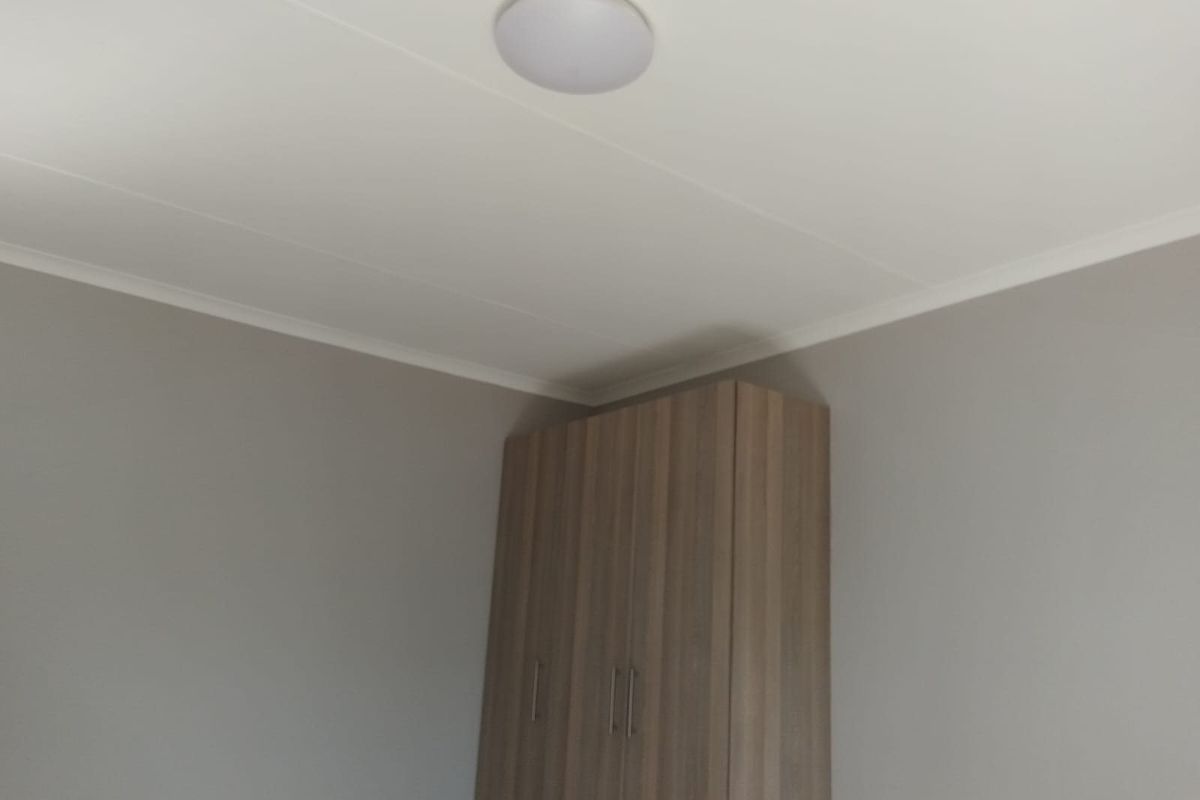 A clean bedroom interior featuring a neutral wall finish, a built-in wooden wardrobe, and simple ceiling lighting.