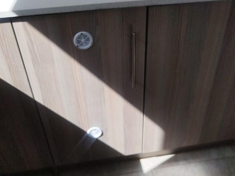 A close-up view of modern kitchen cabinetry featuring wood-grain laminate doors, stone countertops, and integrated ventilation vents.