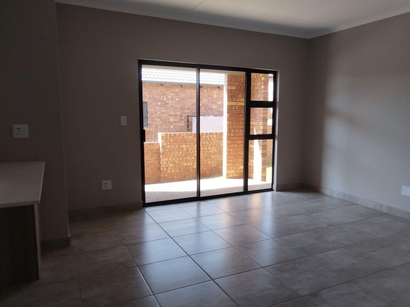 An empty open-plan living area featuring neutral tiled flooring and a large sliding glass door providing access to an outdoor patio space.