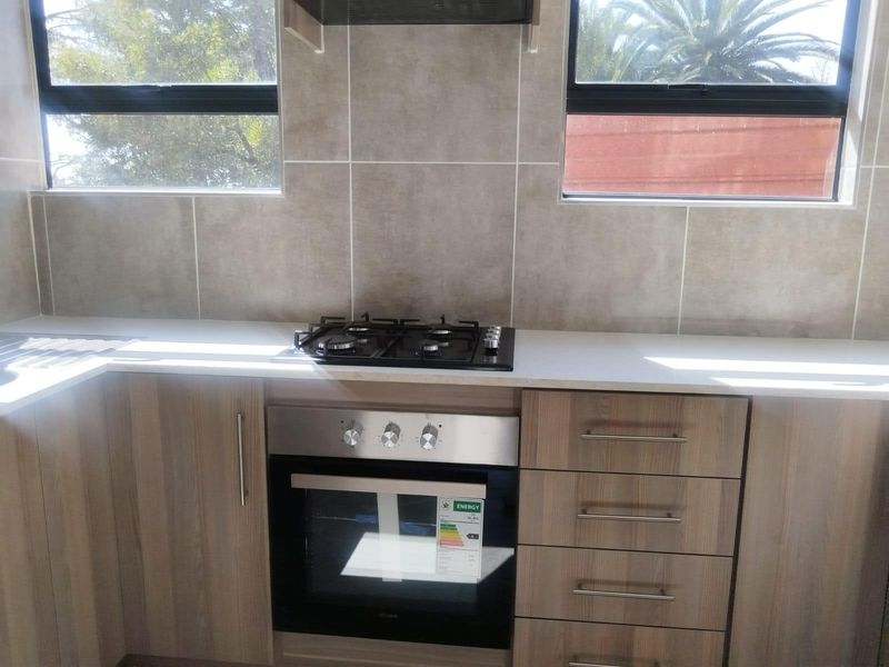 Modern kitchen featuring wood-look cabinetry, stone countertops, a built-in gas hob, and an oven, complemented by a neutral tiled splashback and large windows.