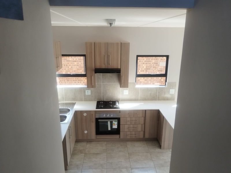 A clean, modern kitchen featuring light wood-finish cabinetry, a gas hob, built-in oven, extractor fan, and neutral tiled flooring.