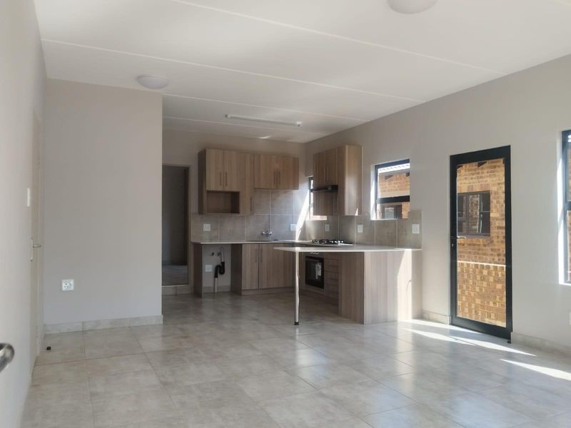 Modern open-plan kitchen and living area featuring neutral tiled floors, built-in cabinetry, and integrated cooking appliances, offering a clean and functional space.