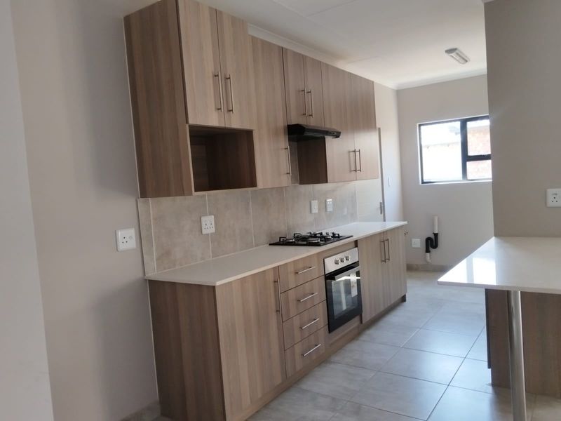 Modern kitchen featuring wood-look cabinetry, stone countertops, built-in gas hob, oven, and extractor fan, with neutral tiled flooring and a breakfast bar.