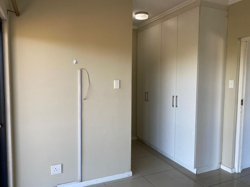A bedroom interior featuring built-in cupboards, tiled flooring, and neutral wall tones, currently vacant and ready for personalization.