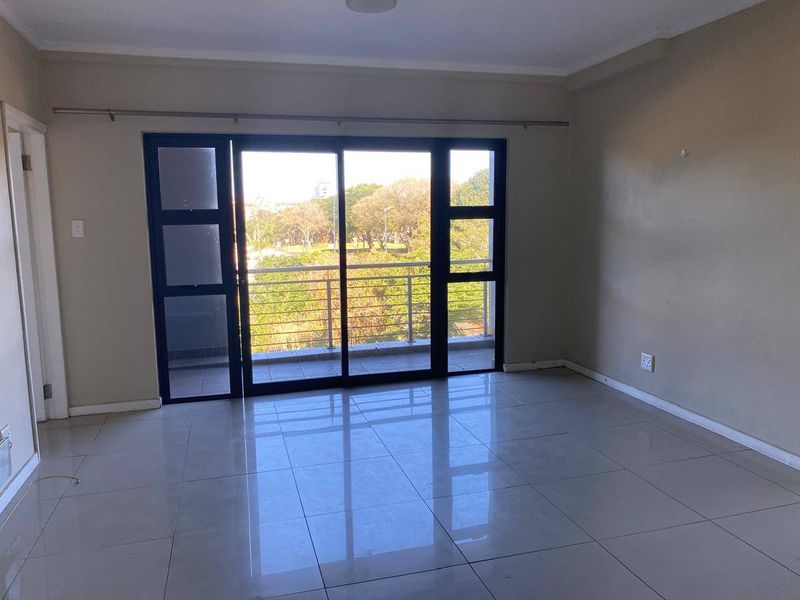 An empty, well-lit living room featuring neutral tiled flooring and large sliding glass doors that provide access to a balcony with scenic views.