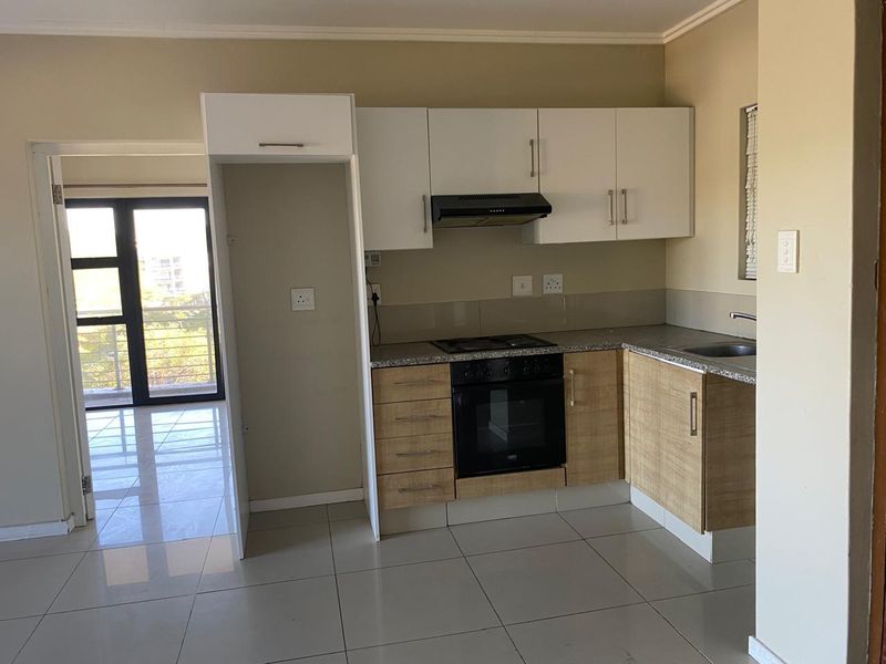 A clean, functional kitchen featuring modern two-tone cabinetry, granite countertops, built-in oven, hob, and extractor fan, with tiled flooring throughout.
