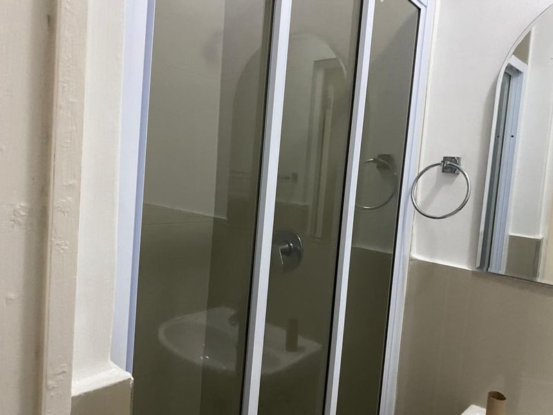 A functional bathroom featuring a shower enclosure, wall-mounted mirror, and chrome fixtures, presenting a clean and simple layout.