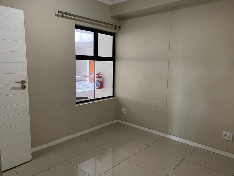 A clean, empty bedroom featuring neutral tiled flooring, an aluminium-framed window, and modern finishes, ready for personalization.