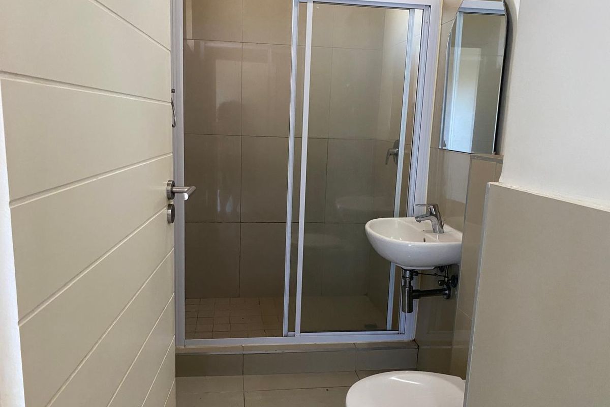 A compact, modern bathroom featuring a glass-enclosed shower, wall-mounted basin, and tiled finishes throughout.