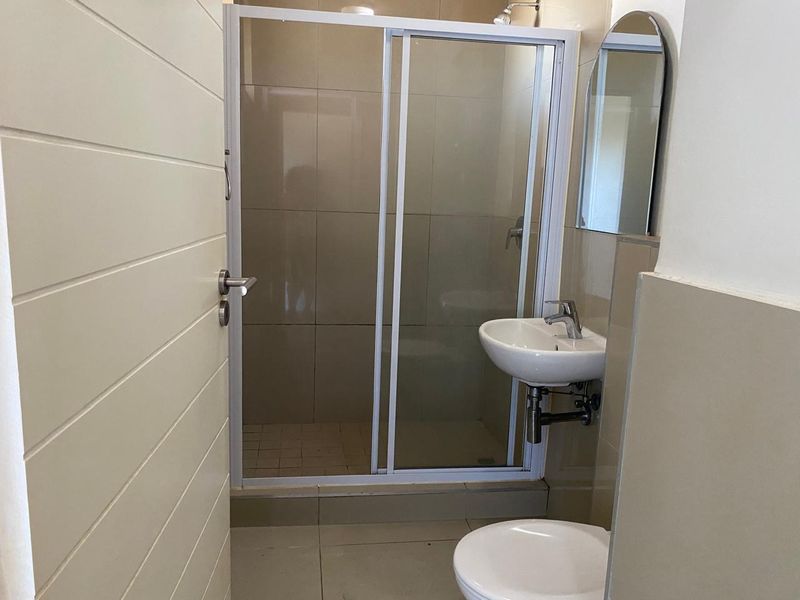A compact, modern bathroom featuring a glass-enclosed shower, wall-mounted basin, and tiled finishes throughout.