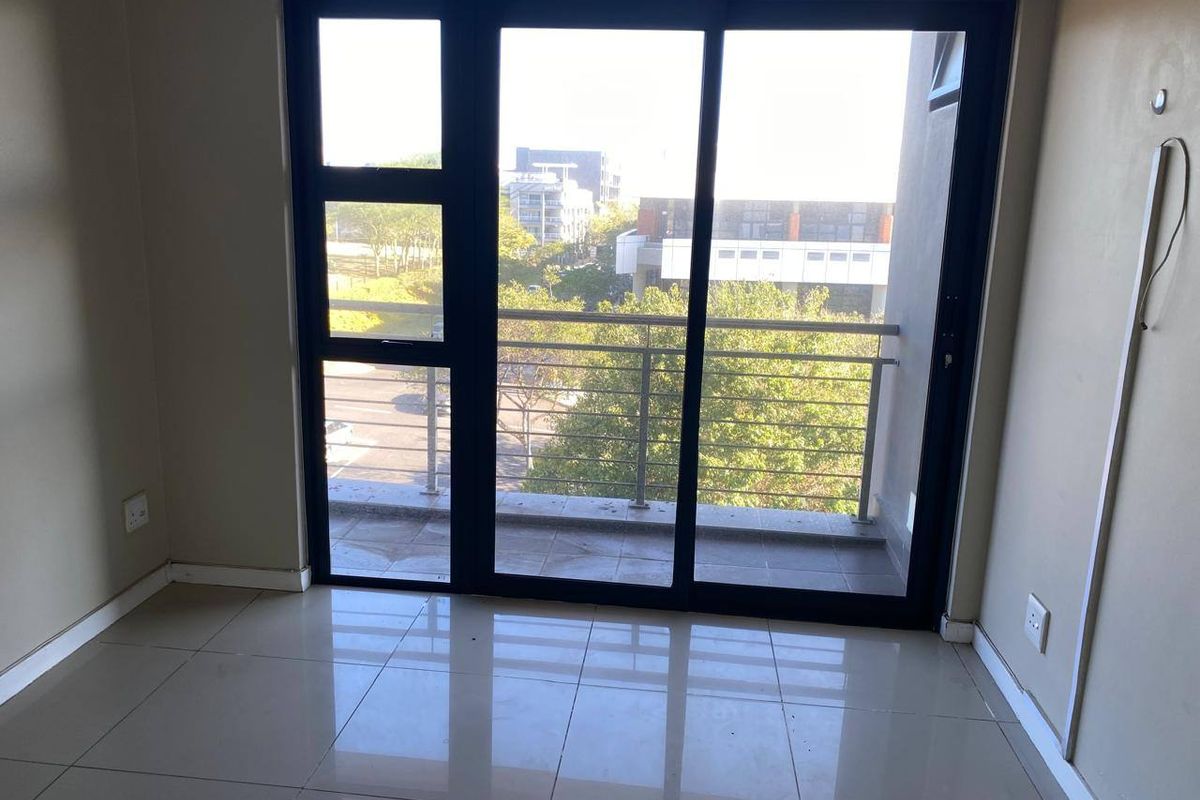An empty living area featuring large sliding glass doors that open onto a private balcony with a stainless steel railing.