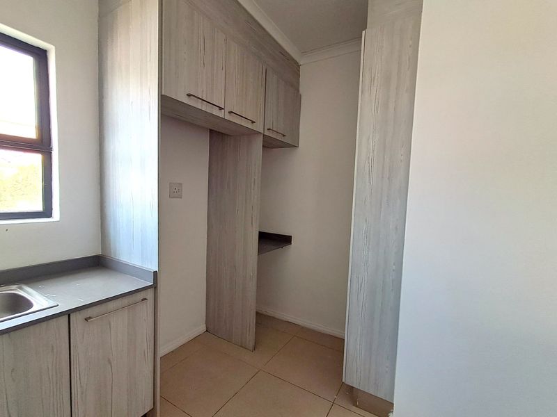 A functional scullery area featuring built-in light wood-grain cabinetry, laminate countertops, a stainless steel sink, and neutral tiled flooring.