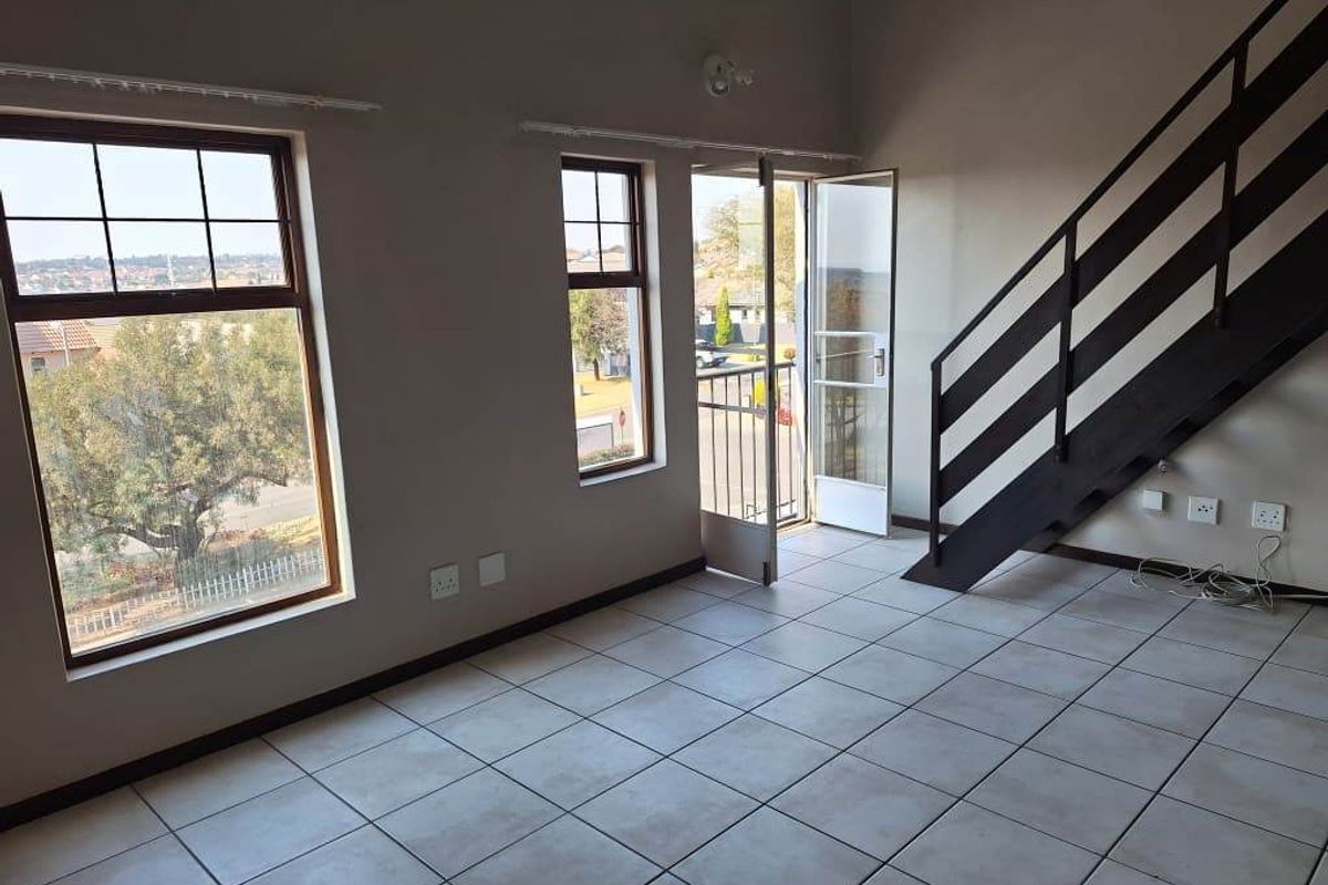 An empty living area featuring tiled flooring, a staircase with a metal railing, and direct access to a balcony through a glass door.