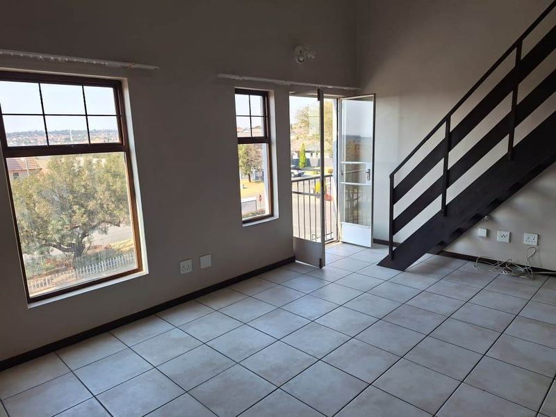 An empty living area featuring tiled flooring, a staircase with a metal railing, and direct access to a balcony through a glass door.
