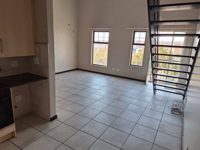 Open-plan living area featuring tiled flooring, a compact kitchen section, and a staircase leading to an upper level with large windows.